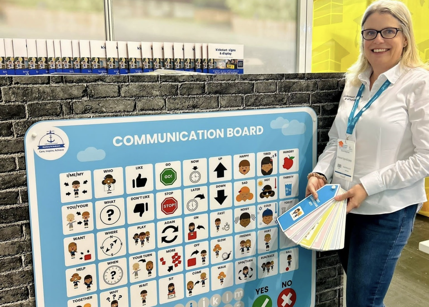 A Voice 4 All employee showcasing the Primary School Communication Board and Primary School Silent Language Key at an exhibition event.